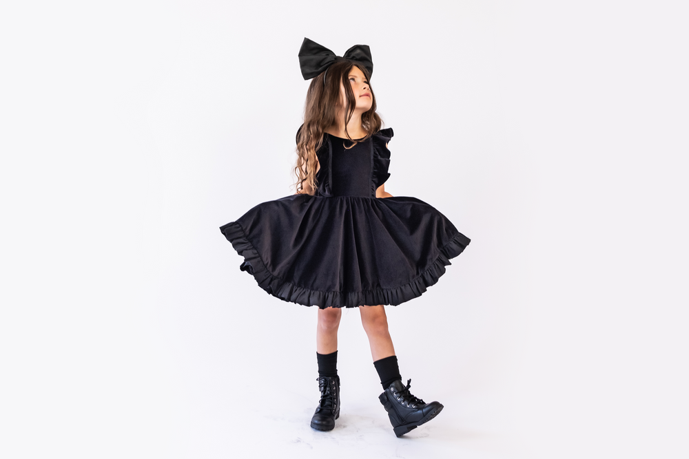 A child posing wearing the black velvet belle a extra large bow on her head