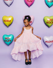 Girl in front of heart candy inspired balloons wearing a pink clip dot cotton ruffle hem high low dress