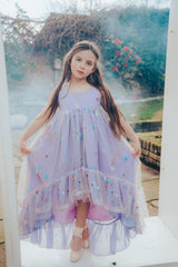Girl in front of a misty background wearing a Pleiades Designs high low dress with embroidered stars and a ruffle hem