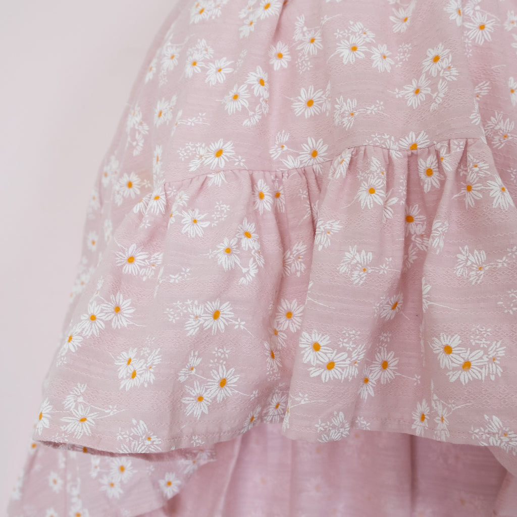 Close up of a Pleiades Designs pink dress with a ruffle hem and a daisy pattern