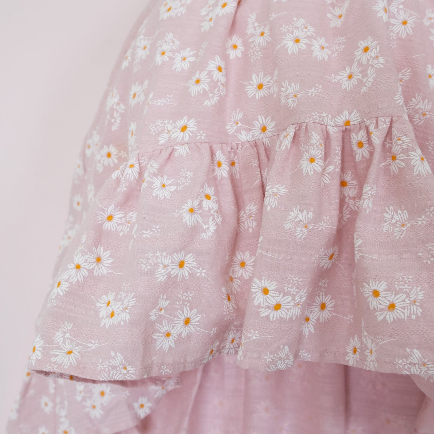 
                  
                    Close up of a Pleiades Designs pink dress with a ruffle hem and a daisy pattern
                  
                