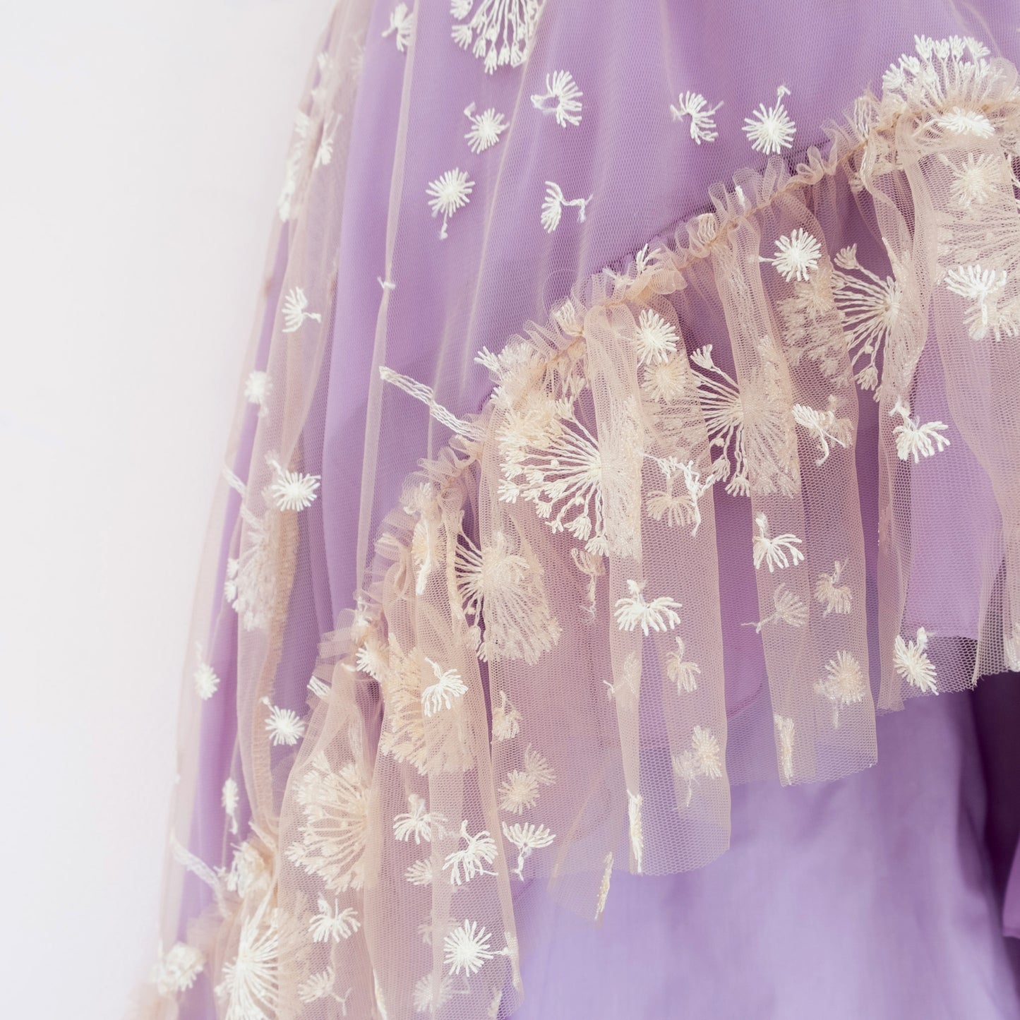 
                  
                    Close up of a Pleiades Designs purple ruffle hem with white embroidered dandelions
                  
                